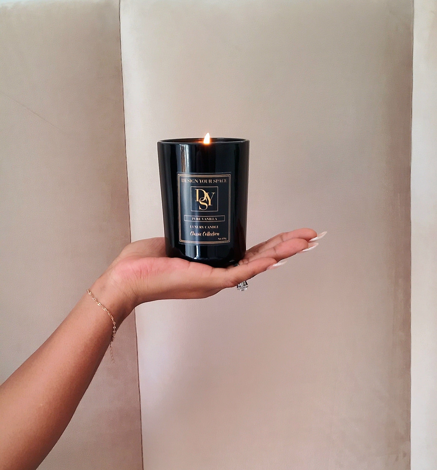 Hand holding a black candle with a visible brand label against a neutral background